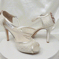 A pair of ivory high heeled platform lace shoes with an ankle strap and a crystal design on the back heel of the peep toe shoes