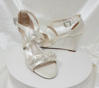 A pair of ivory wedding shoes with high wedge and straps across the front of the foot designed with a pearl and crystal design on the front toe strap of the shoes