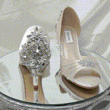 A pair of ivory satin medium height heel bridal shoes with a peep toe and designed with a crystal design on the front of the shoes and a crystal design on the back heel of the shoes