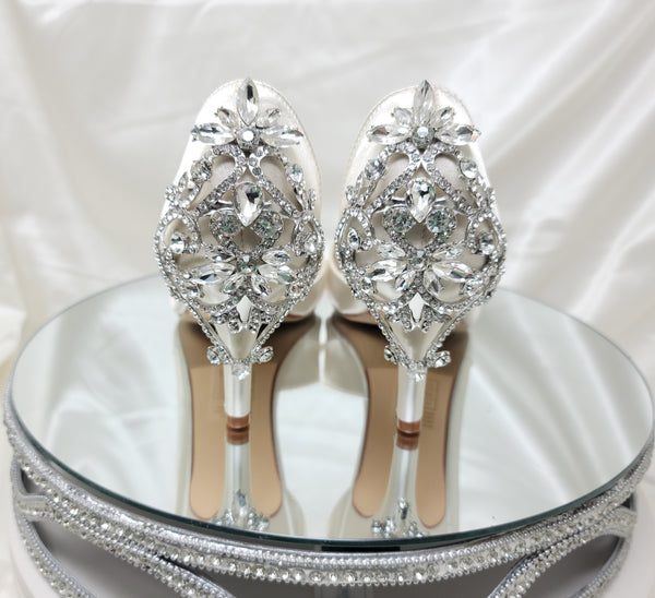 A pair of ivory satin medium height heel bridal shoes with a peep toe and designed with a crystal design on the front of the shoes and a crystal design on the back heel of the shoes