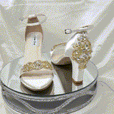A pair of ivory block heel shoes with an ankle strap and a gold crystal design on the front toe strap of the shoes and a gold crystal design on the heel of the shoes