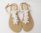 a pair of flat heel ivory bridal sandals with lace flowers on the straps of the sandals