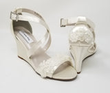 A pair of ivory wedding shoes with high wedge and straps across the front of the foot designed with a lace design on the front toe strap and a lace design on the back heel of the shoes