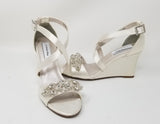 A pair of ivory wedding shoes with high wedge and straps across the front of the foot designed with a crystal design on the front toe strap of the shoes