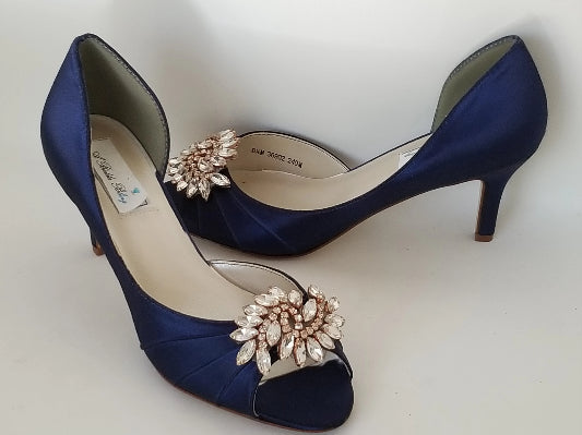 A pair of navy blue satin medium height heel shoes with a peep toe and designed with a rose gold crystal design on the front of the shoes