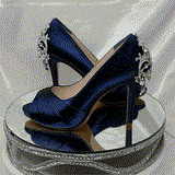 A pair of high heeled navy blue satin shoes with a peep toe and a hidden platform at the front of the shoes and a crystal design on the back heel of the shoes