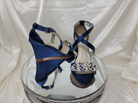 A pair of navy blue wedding shoes with high wedge and straps across the front of the foot designed with a crystal design on the front toe strap of the shoes 
