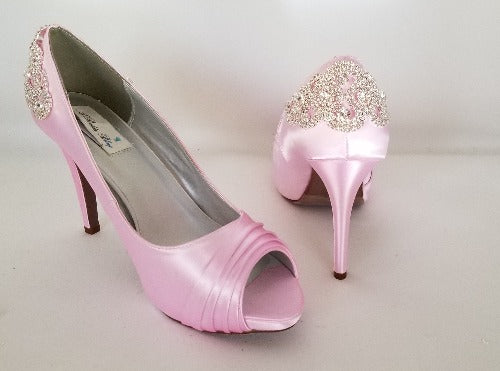 A pair of high heeled pink satin shoes with a peep toe and a hidden platform at the front of the shoes and a crystal design on the back heel of the shoes