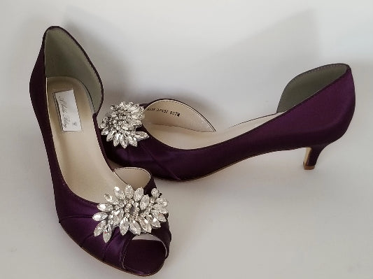 A pair of eggplant purple satin kitten heels with a peep toe and designed with a crystal design on the front of the shoes