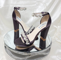 A pair of eggplant purple high block heel platform shoes with an ankle strap and a crystal design on the front toe strap of the shoes and a crystal design on the ankle strap of the shoes