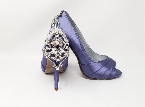 A pair of high heeled lilac purple satin shoes with a peep toe and a hidden platform at the front of the shoes and a crystal design on the back heel of the shoes