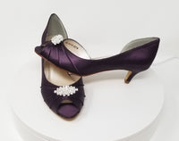 A pair of eggplant purple satin kitten heel shoes with a peep toe with a small crystal design on the front of the shoes
