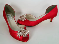 A pair of red satin kitten heel shoes with a peep toe and a crystal design on the front of the shoes
