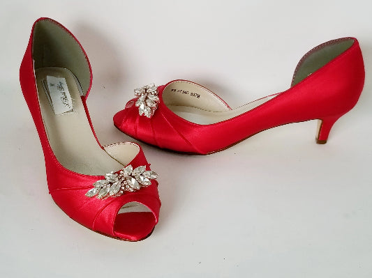 A pair of red satin kitten heel shoes with a peep toe and a rose gold crystal design on the front of the shoes