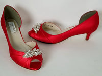 A pair of red satin kitten heel shoes with a peep toe and a crystal design on the front of the shoes