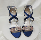 A pair of navy blue wedding shoes with high wedge and straps across the front of the foot designed with a rose gold crystal design on the front toe strap of the shoes 