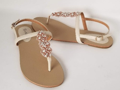 a pair of flat heel ivory bridal sandals with rose gold crystals on the straps of the sandals