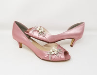 a pair of dusty rose low heel kitten heels with a peep toe and with a pearl and crystal bow design on the side of the shoes
