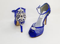 A pair of royal blue high heeled platform lace shoes with an ankle strap and a crystal design on the front of the peep toe shoe and a crystal design on the back heel of the shoes