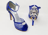 A pair of royal blue high heeled platform lace shoes with an ankle strap and a crystal design on the front of the peep toe shoe and a crystal design on the back heel of the shoes