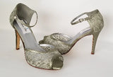 A pair of sage green lace high heeled shoes with a front hidden platform and an ankle strap with a peep toe