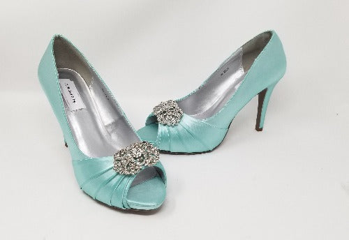 A pair of high heeled aqua blue satin shoes with a peep toe and a hidden platform at the front of the shoes and a crystal design on the front of the shoes