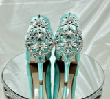 A pair of high heeled aqua blue satin shoes with a peep toe and a hidden platform at the front of the shoes and a crystal design on the front of the shoes and a crystal design on the back heel of the shoes