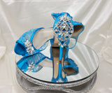 A pair of turquoise high heeled platform lace shoes with an ankle strap and a crystal design on the front of the peep toe shoes and a crystal design on the back heel of the shoes