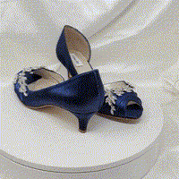 A pair of  bridal shoes in navy blue satin with a kitten heel and a peep toe and a crystal bow design on the front of the shoes