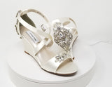 A pair of ivory wedding shoes with high wedge and straps across the front of the foot designed with a crystal design on the front toe strap and a crystal design on the back heel of the shoes