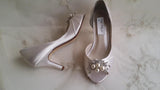 A pair of ivory satin wedding heels with a peep toe and designed with a crystal and pearl design on the front of the shoes 