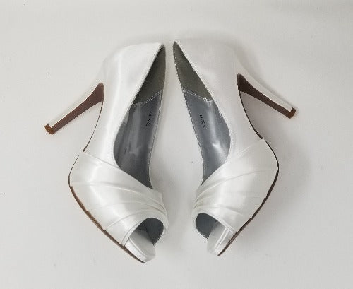 A pair of high heeled white satin shoes with a peep toe and a hidden platform at the front of the shoes