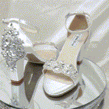 A pair of white block heel shoes with an ankle strap and a crystal design on the front toe strap and a crystal design on the back heel of the shoes
