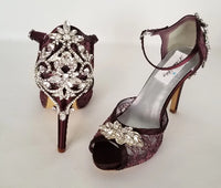 A pair of wine high heeled platform lace shoes with an ankle strap and a crystal design on the front of the peep toe shoes and a crystal design on the back heel of the shoes