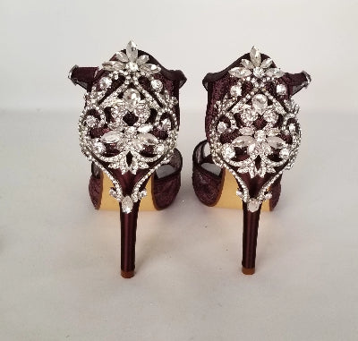 A pair of wine high heeled platform lace shoes with an ankle strap and a crystal design on the front of the peep toe shoes and a crystal design on the back heel of the shoes